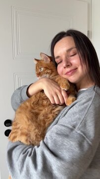 Girl brunette hugging and dancing with cute orange domestic cat at home