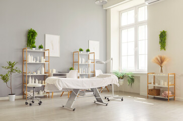 Obraz premium Sunny spa salon clinic interior with a height adjustable treatment table, cosmetic shelves, and cosmetology exam lamp, styled for wellness in calm, minimal design. Skin care and beauty day concept.