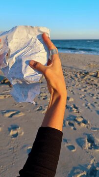Crumpled Letter Held Toward Ocean. Hand holds a crumpled handwritten letter toward the ocean representing letting go of pain and emotional healing.