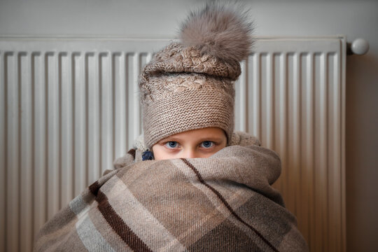 Frozed Child in Cold Home near Heater Radiator due to Blackout. Energy Crisis in Ukraine concept. 