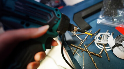Electric Drill in Hand with Multiple Drill Bits Laid Out on Surface