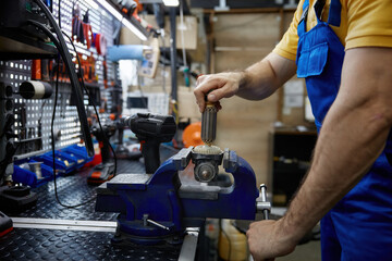 A skilled man is working on broken electrical equipment that is securely clamped in a vise