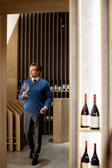 Obraz premium Man in blue sweater enjoys wine tasting at elegant winery in modern decor