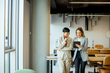 Two colleagues discuss a project in a modern office setting during the workday