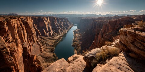 Breathtaking view of a canyon river bend with red rock cliffs and a bright sunburst in a clear blue sky, showing majestic landscape nature.