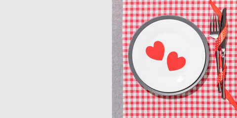 Romantic Table Setting with Red Paper Hearts on White Plate, Cutlery with Ribbon, and Gingham Napkin. Holiday Concept for Valentine's Day Dinner, Dating, Anniversary or Love Visuals with Copy Space