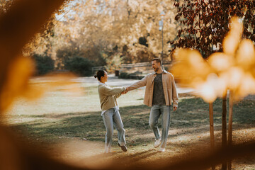 Korean woman and Caucasian man share a joyful moment while walking in a sunny autumn park