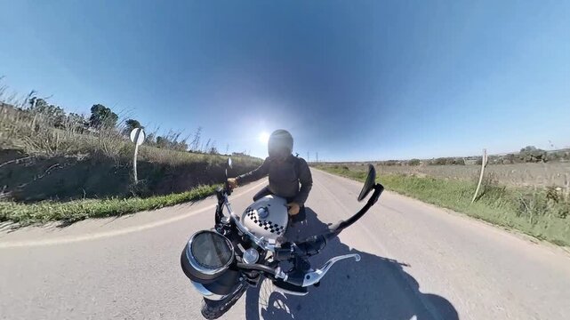 Chico con casco oscuro en motocicleta cl&aacute;sica rodando por carretera y bosque en d&iacute;a soleado ,toma grabada en 4k