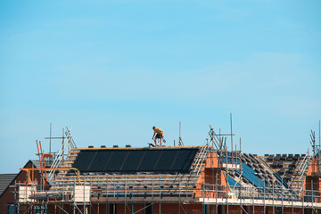 Fototapeta premium Construction worker stands on top of the roof while installing new solar panels in bright sunlight