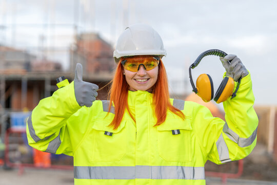 Concept of standard safety PPE to be used on construction site. Woman builder shows ear defenders