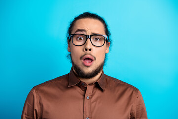 Obraz premium Portrait of a surprised young man in glasses wearing a brown shirt against a teal background
