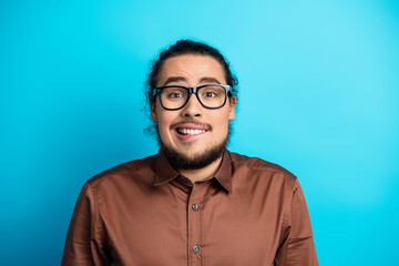 Fototapeta premium Portrait of a young man wearing glasses and a brown shirt, posing on a teal background, expressing a humorous and lively demeanor