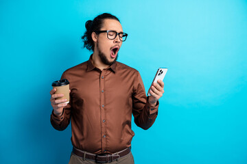 Young businessman yawning with coffee and smartphone against a vibrant teal background showcasing daily moments