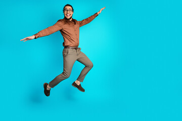 Fototapeta premium Joyful young businessman jumping energetically against a bright teal background showcasing delight and positivity