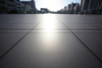 Light shines on the tiled walkway in the city during the early morning hours with buildings in the background