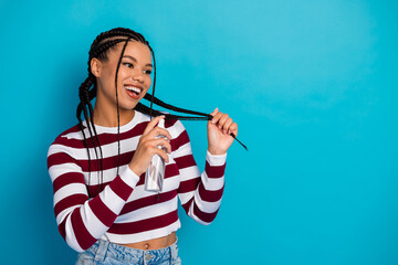 Young woman with braids sprays perfume in a bright blue studio smiling warmly in a casual striped...