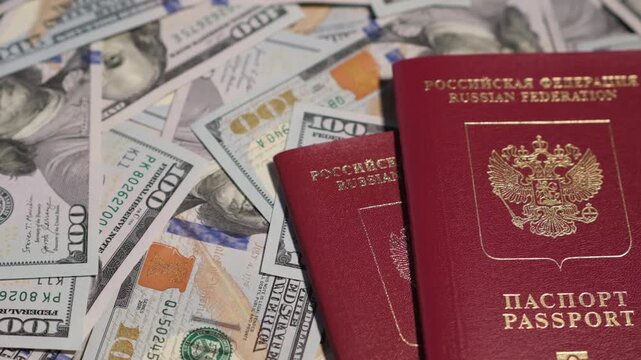 Close-up view shows Russian passports placed on top of numerous US dollar bills, highlighting the contrast between currencies.