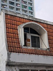 Arched Dormer Window on Red Tile Roof Against Modern High-Rise Building