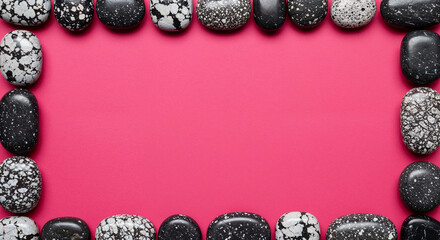 Decorative border frame made of speckled black and white river stones arranged on a solid vibrant pink background with copy space in the center.