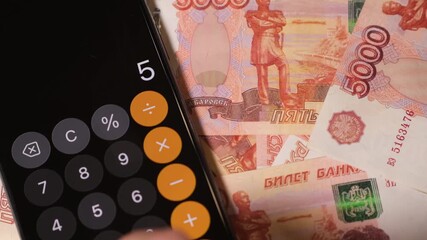 Displaying a close-up of a calculator entering amounts while surrounded by Russian banknotes under natural light. - Powered by Adobe