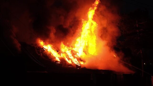 A house experiences a severe fire with bright flames and dark smoke rising into the night sky, causing chaos in the neighborhood.