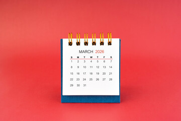 March 2026 white desk calendar on red background.