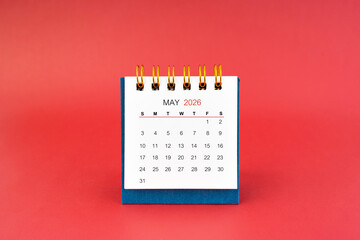 May 2026 white desk calendar on red background.