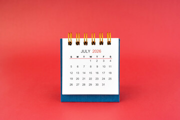 July 2026 white desk calendar on red background.