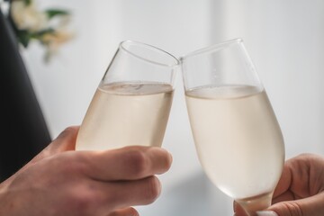Caucasian middle aged man and Caucasian middle aged woman clinking champagne glasses during celebration, both hands visible holding drinks in bright indoor setting