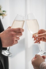 Caucasian middle aged man and Caucasian middle aged woman clinking champagne glasses during celebration, both hands visible holding drinks in bright indoor setting