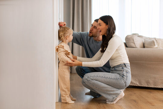 Kids Growth Progress. Loving parents fixing height of sweet little daughter child, setting hand on wall over kids head