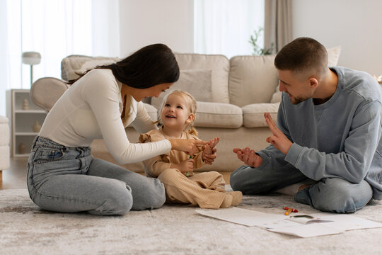 Warm Family Time. Happy parents playing with little daughter, teach to count on fingers while sitting on the floor in living room