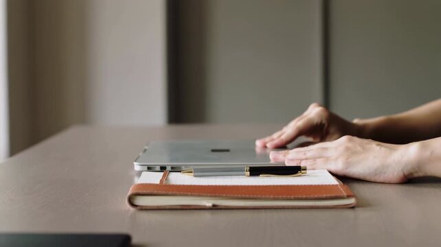 Hands opening and closing laptop on desk with notebook and pen, natural light, clean composition
