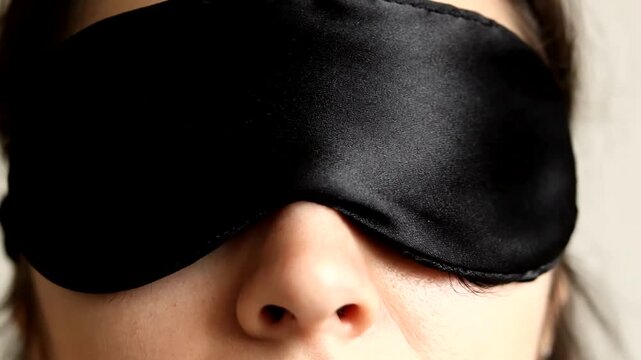 Close up of a person wearing a black silk sleep mask.