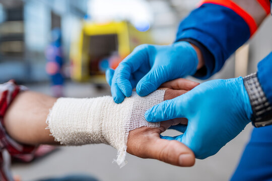 A paramedic, wearing gloves, is applying bandage to person's arm after minor injury during accident