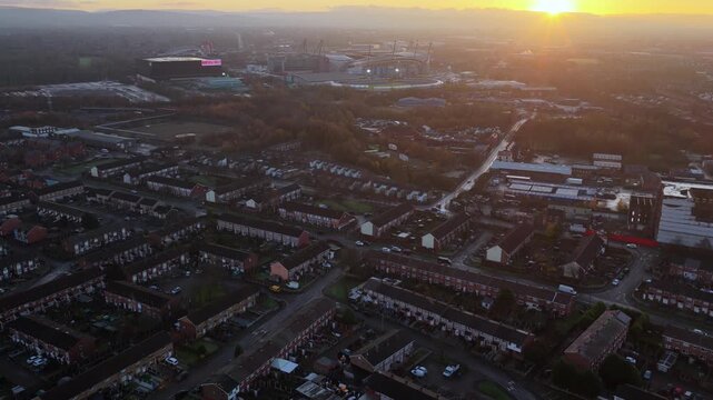 Aerial video looking west from Miles Platting and Beswick toward the Manchester city center at sunrise, featuring modern housing regeneration and the distant Etihad Stadium.