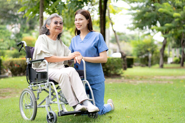 Young caucasian nurse comforting with patient while sitting on wheelchair in outdoor park, doctor woman support and counseling with patient, caregiver and service with senior, medical and consoling.
