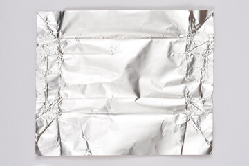 A square sheet of crumpled shiny silver aluminum foil centered on a plain gray surface