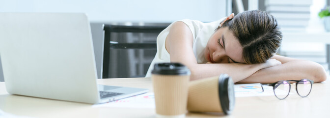 Young businesswoman overworked sleeping on desk with coffee cup in office. Tired business Asian...