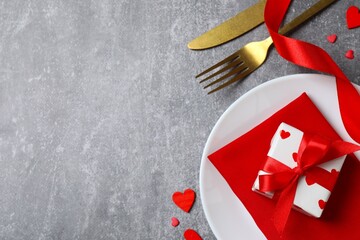 Top view of cutlery with a napkin, plate, gift box and decorative hearts on a gray table with space for text. Valentine's Day romantic dinner