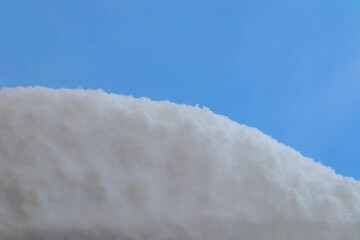 A close-up view of a snow-covered surface under a clear blue sky. The snow appears soft and fluffy, creating a serene winter scene.