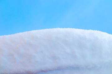A close-up view of a snow-covered surface under a clear blue sky. The snow appears soft and fluffy, creating a serene winter scene.