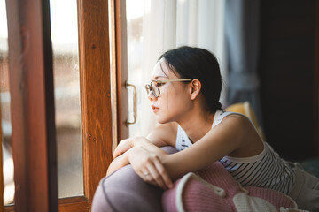 Lonely woman looking out window in living room apartment sadness mood unhappy waiting for someone...