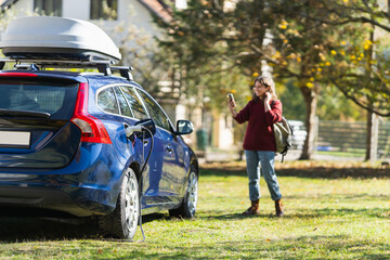 Woman traveler with smartphone next to charging electric car on backyard of country house