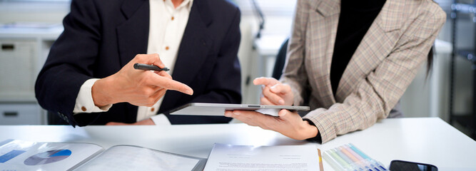 businesswoman and businessman analyzing financial charts and discussing business strategy at desk, both holding pens and reviewing printed documents together