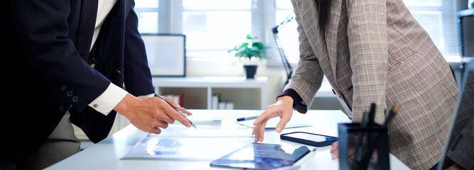 businesswoman and businessman analyzing financial charts and discussing business strategy at desk, both holding pens and reviewing printed documents together