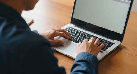 Keyboard Command: A focused individual intently works at a sleek laptop on a smooth wooden desk, his fingers dancing over the keys, highlighting the process of digital interaction.