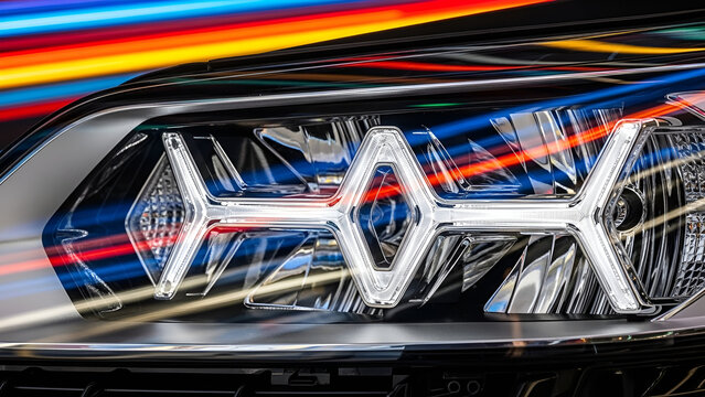 Futuristic LED Car Headlight Detail with Dynamic Geometric Design Against Colorful Speeding Light Trails.