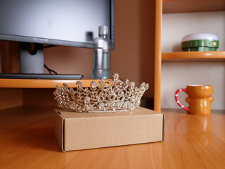Silver decorative crown resting on cardboard box on wooden table in home interior.