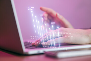 Hands typing on a laptop with digital graphs and numbers showing future years in a workspace setting
